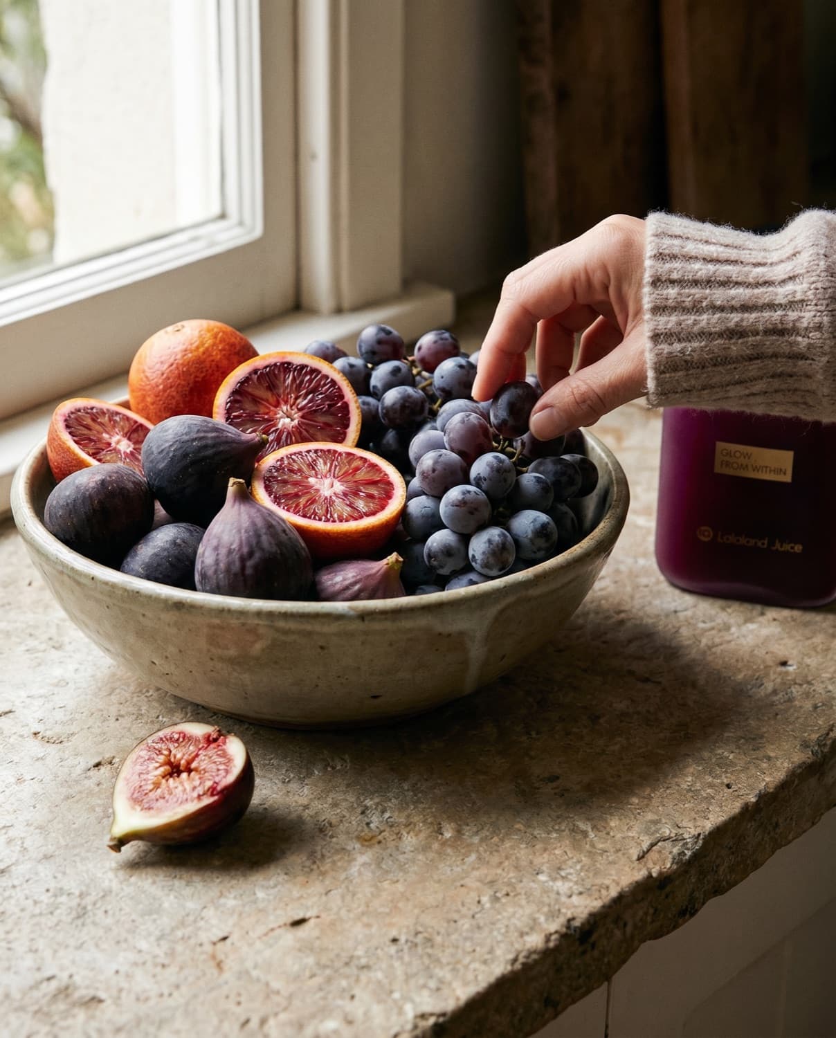 An overflowing bowl of figs, blood oranges and grapes with a Lalaland bottle nearby