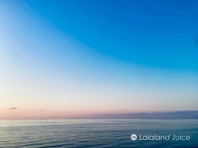 First light over a calm sea, the horizon turning rose before the 7:06 sunrise — with the Lalaland Juice mark set within.