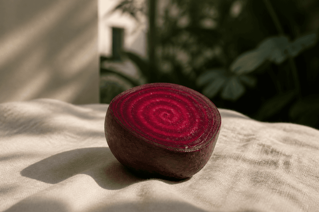 A single beetroot halved on pale linen, its concentric ruby growth rings glowing in low afternoon light.
