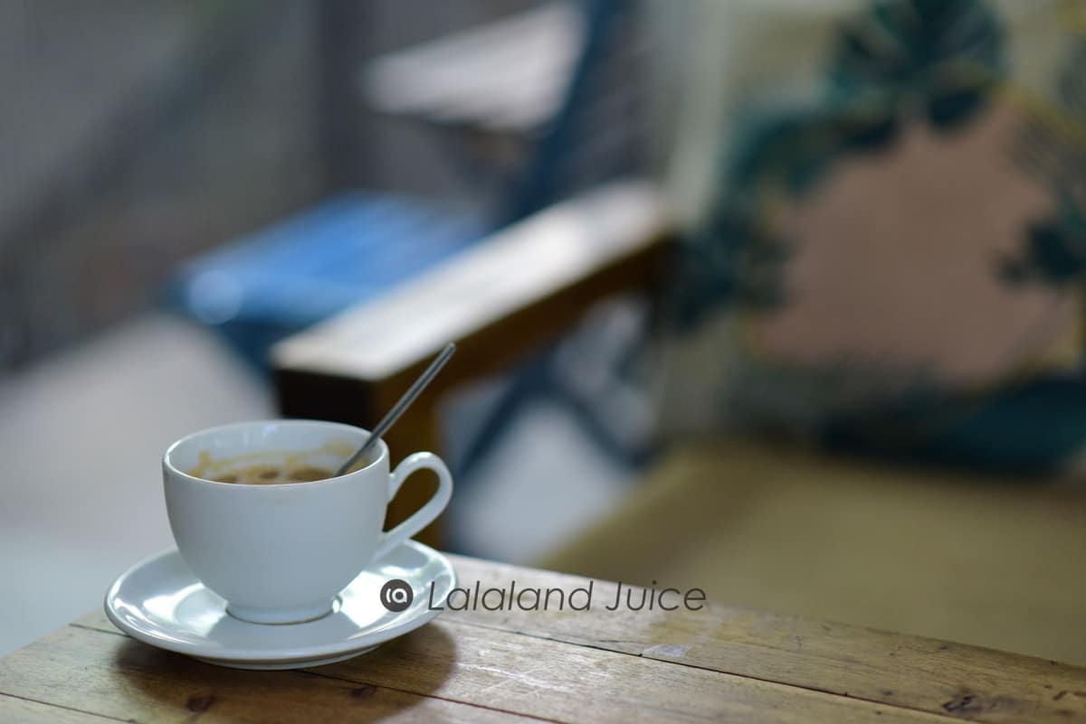 A warm cup of coffee on a sunlit wooden table in a calm cafe — the three-o'clock hour, met with a pause rather than a fourth kopi.