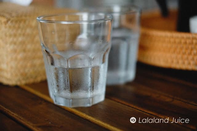 A cold glass beading with condensation on a warm wooden table in soft afternoon light, the Lalaland Juice mark set quietly within.