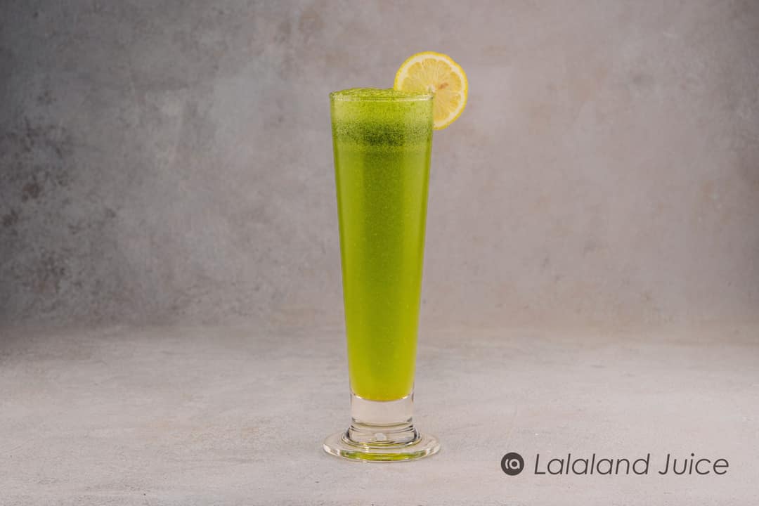 A tall glass of cold green juice with a slice of lemon.