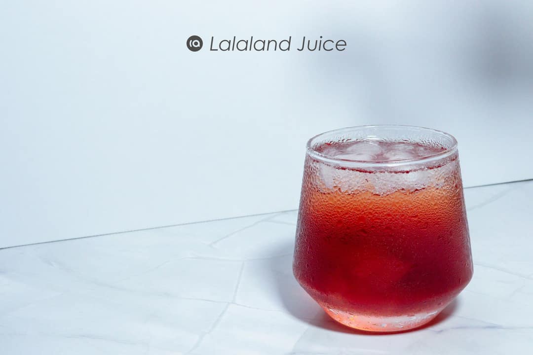 A cold blush-red drink sweating in a clear glass on a pale table — the pour that marks the end of the day.