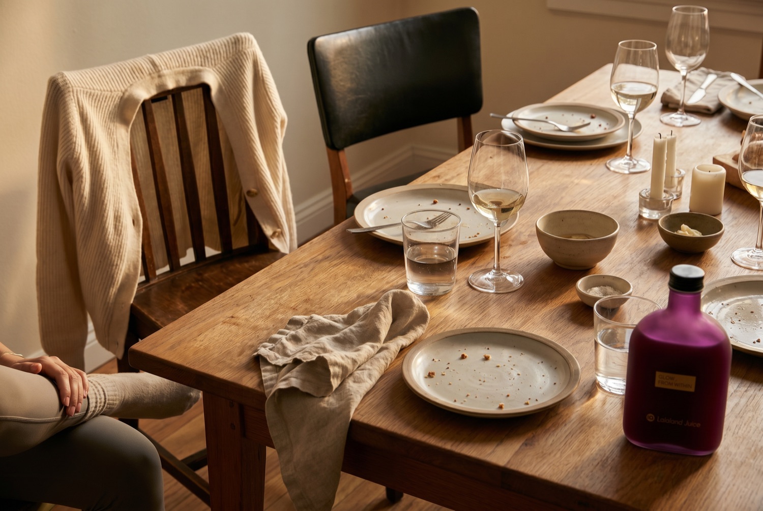 A table after friends have left, half-drunk glasses and a Lalaland bottle in warm light